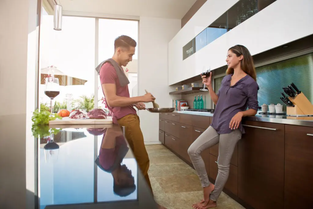 Couple chatting and drinking wine whilst cooking in kitchen.